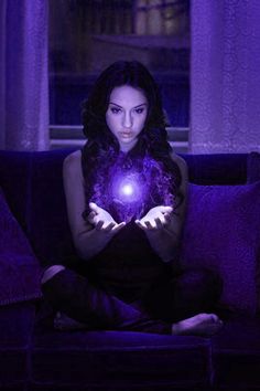 a woman sitting on a couch holding a glowing ball in her hands and looking at the camera