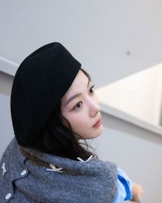 a young woman wearing a black hat and gray sweater is looking off to the side