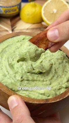 a person dipping something into a wooden bowl filled with guacamole and bacon