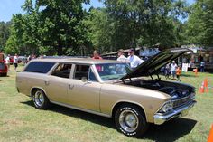 an old station wagon with its hood open at a car show on the grass in front of other cars