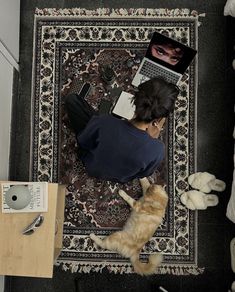 a woman is sitting on the floor with her laptop and cat looking down at it