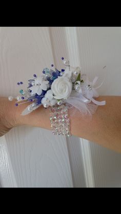 a wrist corsage with white and blue flowers on it, along with crystal beads