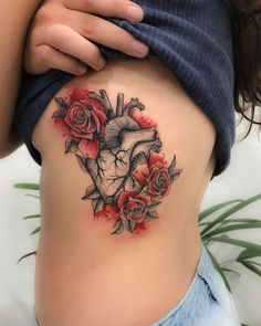 a woman's stomach with roses and a heart tattoo on her side ribcage