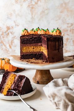 a slice of chocolate cake on a plate with the rest of the cake in the background