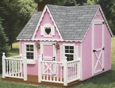 a pink and white doll house in the grass with a porch, fence, and door