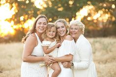 three women and a child are posing for a photo in a field with the sun setting behind them