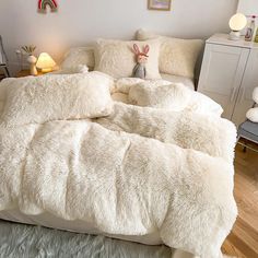 a bed with white fluffy blankets and pillows on top of it, next to a night stand