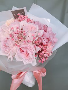 a bouquet of pink flowers is wrapped in white paper and tied to a gray background