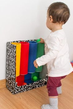 a toddler playing with toys in a playroom on the wooden floor next to a white wall