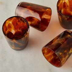 four brown glass cups sitting on top of a white counter next to an orange vase