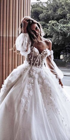 a woman in a white wedding dress standing next to columns with her hands on her head