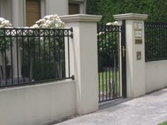 an iron gate with white flowers on it next to a sidewalk in front of a house