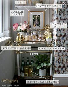 a gold bar cart with lots of bottles and flowers on it in front of a window