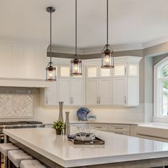 a large kitchen with white cabinets and marble counter tops, along with two pendant lights hanging over the island