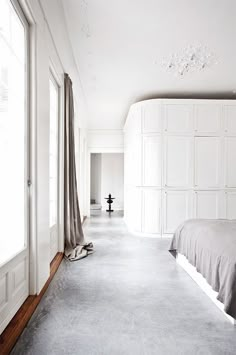 a bedroom with white walls and flooring has a gray blanket on the bed next to it