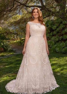 a woman in a wedding dress standing on grass with trees and bushes behind her, smiling at the camera