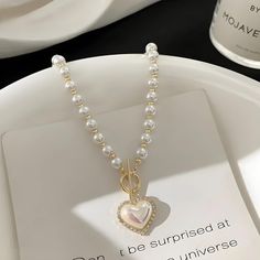 Drape yourself in elegance with this Coquette Heart Pearl Necklace. Lustrous pearls meet a charming heart pendant, creating a timeless piece that adds a romantic glow to any ensemble. Perfect for those seeking a blend of classic grace and endearing charm. Coquette aesthetic Heart shaped pearl with rhinestone pendant Pearl beaded design Zinc alloy Pearl Necklace With Heart Pendant, Silver Pearl Necklace With Heart Charm, Coquette Pearl Necklace, Silver Pearl Heart Pendant Necklace, Silver Pearl Heart Necklace For Valentine's Day, Silver Pearl Necklace For Valentine's Day, Valentine's Day Silver Pearl Heart Necklace, Valentine's Day Pearl Necklace For Party, White Heart-shaped Necklace With Pearl Chain