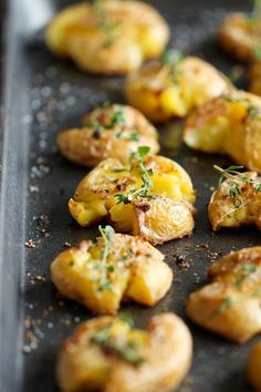 potatoes with herbs and seasoning on top sit on a baking sheet, ready to be cooked