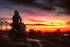 a man riding on the back of a motorcycle next to a train track at sunset