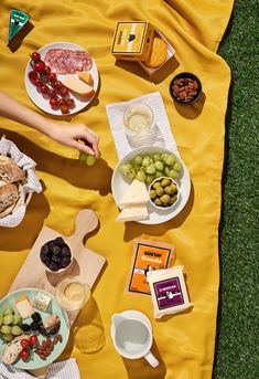 an overhead view of food on a yellow picnic blanket, with cheeses and olives