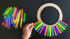 a person holding a wooden circle with colored sticks in front of it and an object made out of popsicle sticks