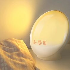 an alarm clock sitting on top of a bed next to a pillow and lamp shade