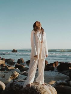 a woman standing on top of a rock next to the ocean with her eyes closed