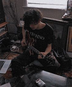 a man sitting in front of a laptop computer while playing an electric guitar on top of a table