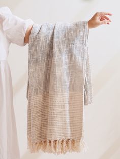 a woman holding up a white and beige blanket with tassels on the ends