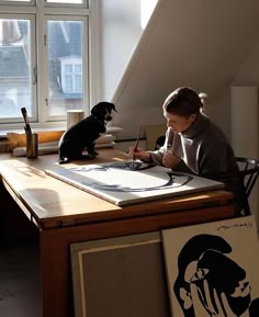 a woman sitting at a table with a dog and some art work on the table