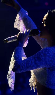 a woman in a white dress is holding a microphone and singing into the air at a concert