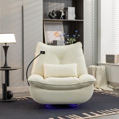 a white chair sitting on top of a blue rug next to a lamp and bookshelf