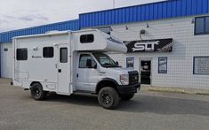 a white truck parked in front of a building with a camper attached to it