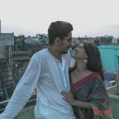 two people standing next to each other on top of a roof with buildings in the background