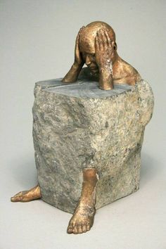 a bronze statue of a person sitting on top of a rock with their head in his hands