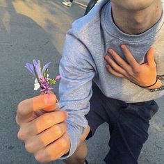 a man holding a small purple flower in his right hand and smiling at the camera