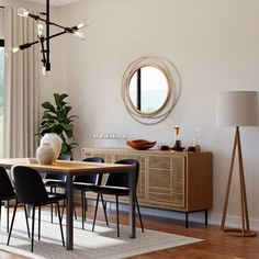 a dining room table with black chairs and a round mirror