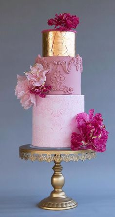 a pink and gold wedding cake with flowers on top