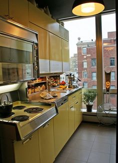 a kitchen with yellow cabinets and stainless steel appliances in front of a large window overlooking the city