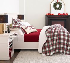 a bedroom decorated for christmas with red and white bedding, plaid comforter, holiday decor