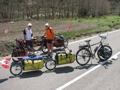 two people standing next to their bikes on the side of the road with luggage strapped to them