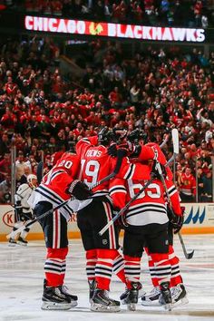 hockey players huddle together on the ice in front of an arena full of fans