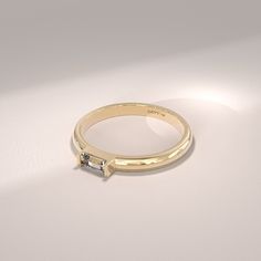 a gold ring with a baguettte cut diamond on the side, sitting on a white surface