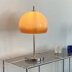 a table lamp sitting on top of a glass shelf next to a cup and mug