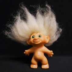 a troll doll with white hair and blue eyes on a black background in front of the camera