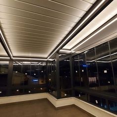 an empty room with lots of windows and lights on the ceiling is lit up at night