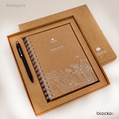 two notebooks and pen sitting on top of a brown box with flowers drawn on it