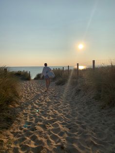 a person carrying a surfboard down a sandy path to the beach at sunset or dawn