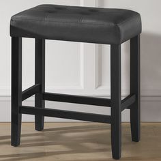 a black leather stool in front of a white wall and wooden flooring with an open door