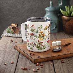 a coffee mug sitting on top of a wooden table next to a spoon and potted plant